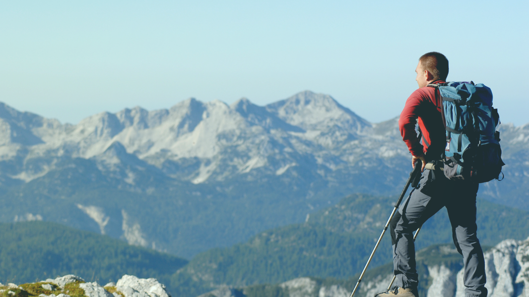 Wanderer mit Rucksack blickt auf ein Bergpanorama.