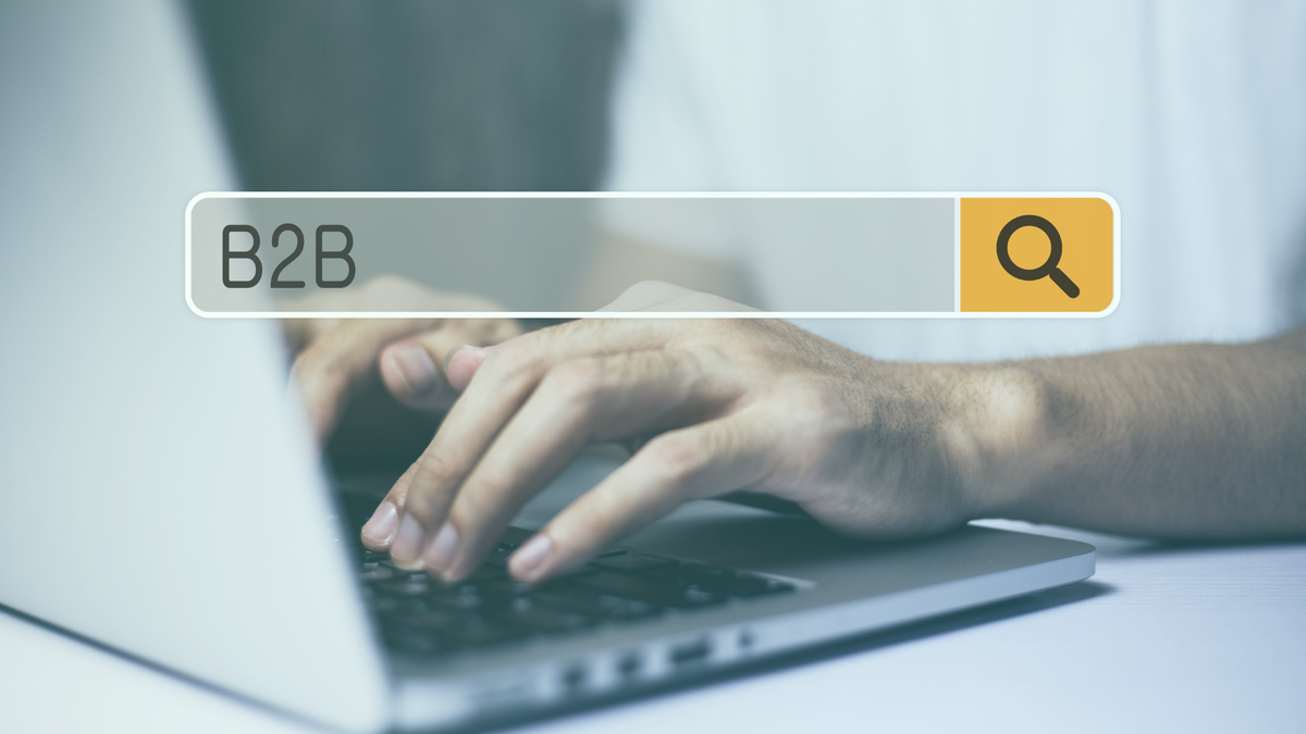 Hände, die auf einer Laptop-Tastatur tippen mit einer drüber gelegten Suchleiste mit der Suche "B2B"