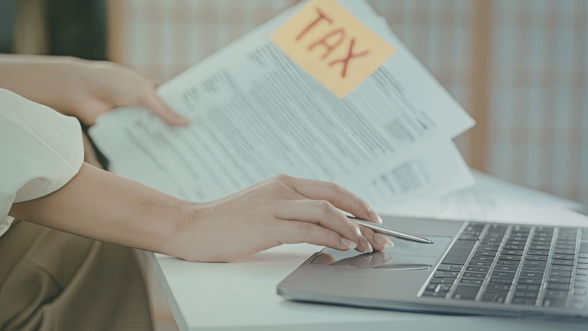 Person bedient Laptop im Hintergrund Blätter mit "TAX" drauf